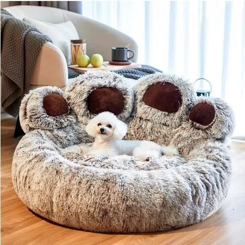 Fluffy paw-shaped pet bed with a small white dog inside, in a cozy living room setting.